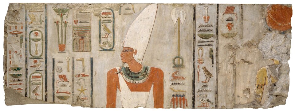 Na zdjęciu znajduje się fragment ścianie ozdobionej licznymi hieroglifami oraz podobizną faraona Mentuhotepa drugiego. Ma on wysoką białą koronę, długą przystrzyżoną bródkę i jest ubrany w białą szatę. Na szyi ma liczne kolorowe naszyjniki. 