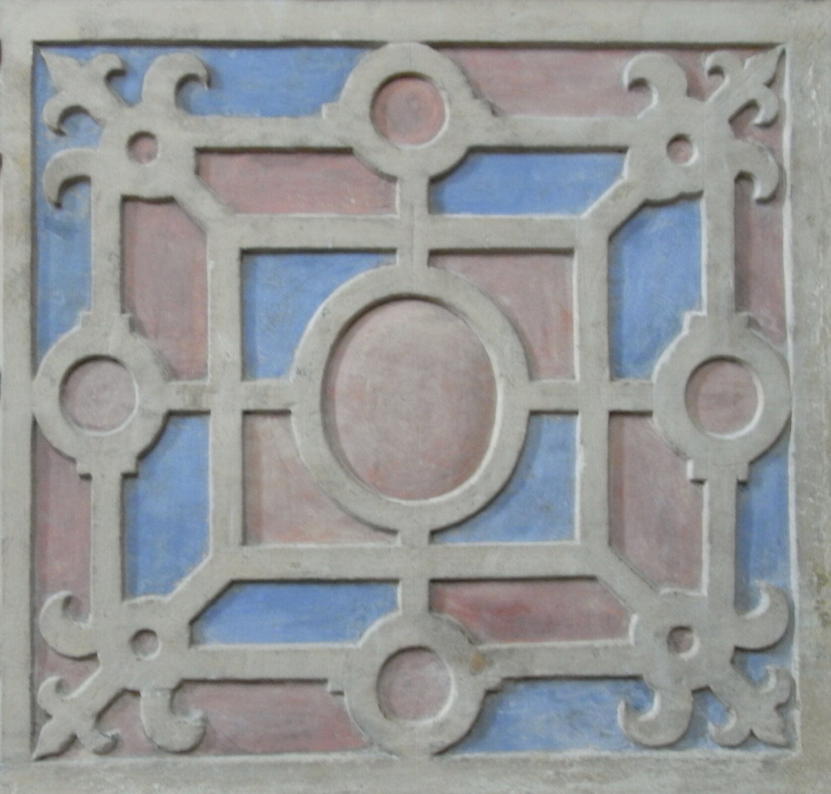 Ilustracja przedstawia ornament okuciowy. Ornament wykonany jest w kształcie kwadratu. W jego centralnym punkcie znajduje się okrąg. Dookoła niego naprzemiennie widoczne są okręgi oraz krzyże z zaokrąglonymi końcami. Wszystkie elementy połączone się liniami.