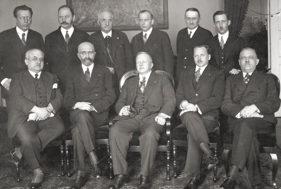 Czarno‑biała fotografia przedstawia członków prezydium BBWR. Mężczyźni ubrani w garnitury pozują do zdjęcia, niektórzy z nich siedzą na krzesłach, a inni stoją za nimi. Za nimi na ścianie wisi obraz. 