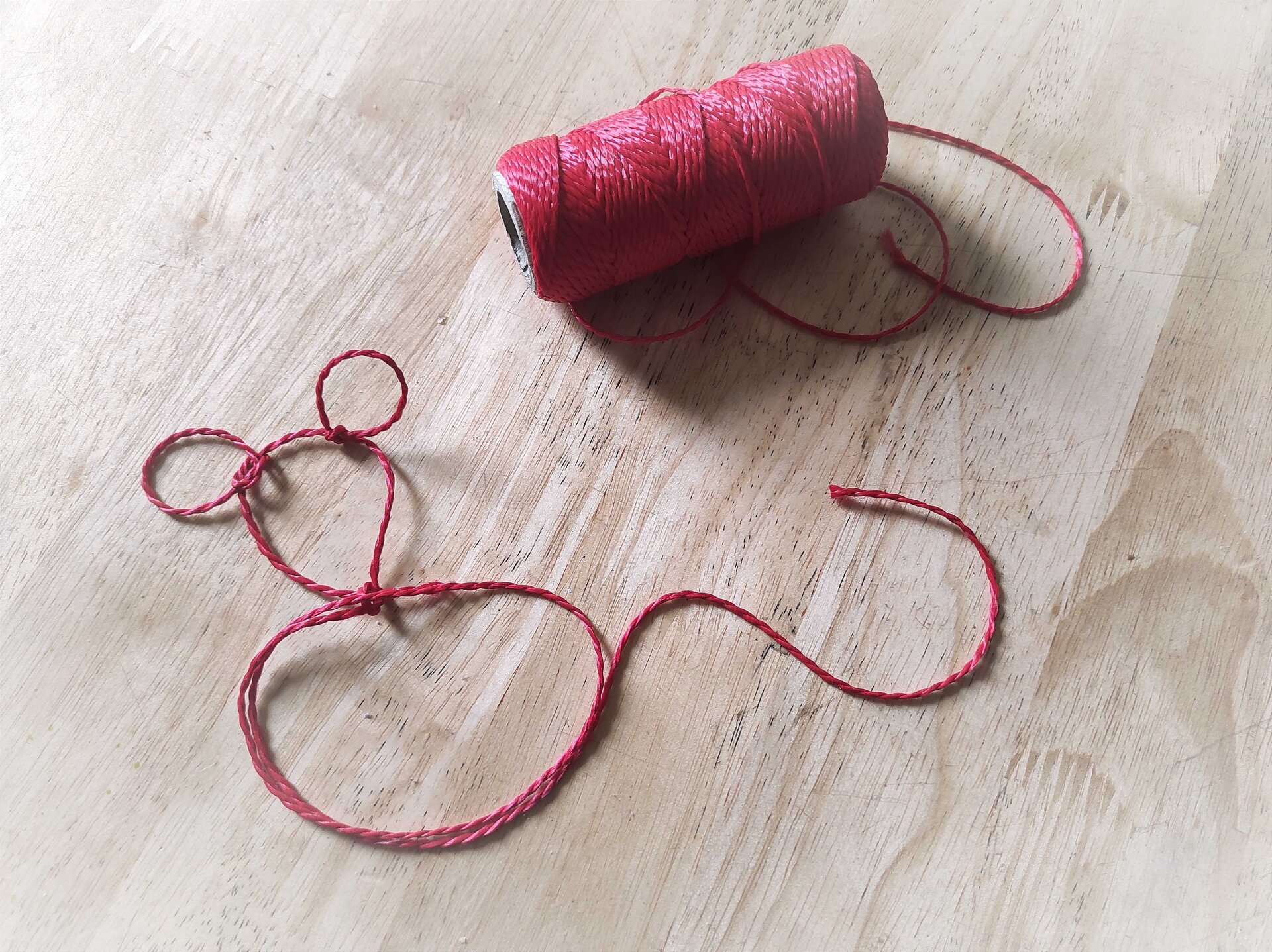 Ilustracja przedstawia czerwoną włóczkę, która ułożona została w kształt myszy.