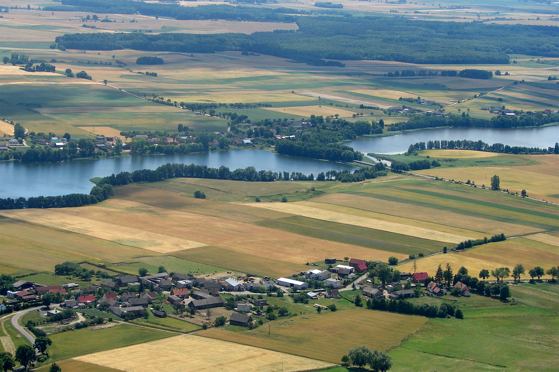 Fotografia wykonana z lotu ptaka ukazuje jeziora Pojezierza Wielkopolskiego. Wokół jezior widoczne liczne pola i łąki.