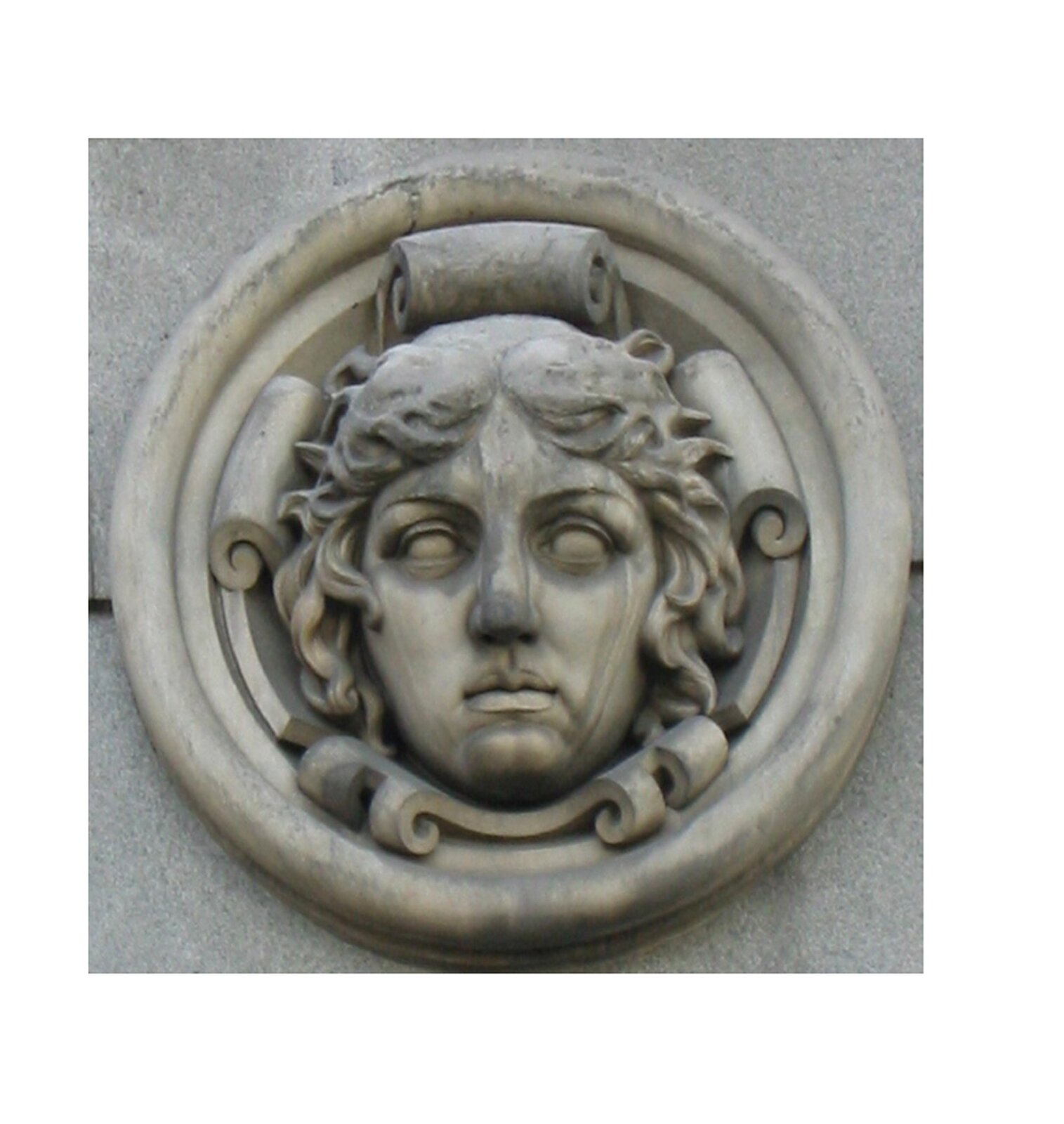 Ilustracja przedstawia ornament – medalion. Ten element dekoracyjny przedstawia twarz młodej kobiety z krótkimi kręconymi włosami. Element ten jest okrągły i znajduje się prawdopodobnie na ścianie.