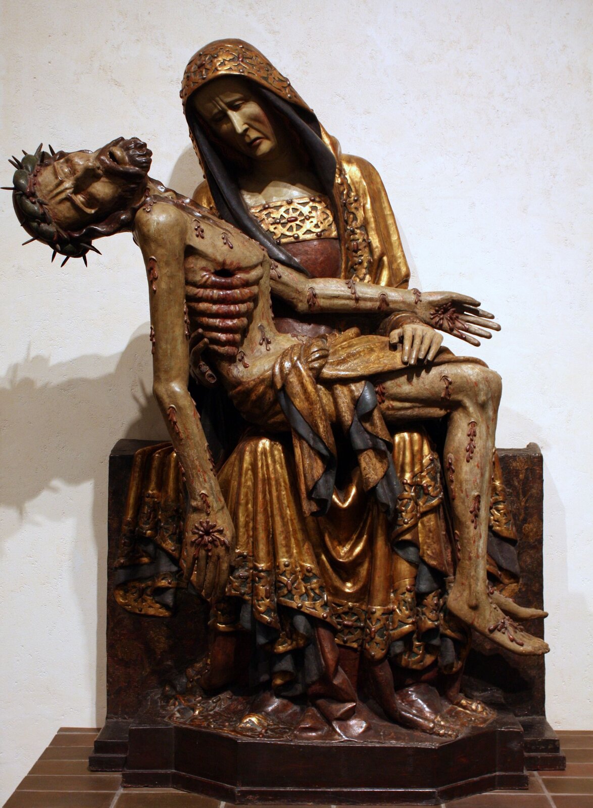 Ilustracja przedstawia figurę, na której Matka Boska opłakuje śmierć Jezusa. Maryja ubrana jest w złote szaty, ma także złoty kaptur. Na jej kolanach spoczywa ciało Chrystusa – poranione, z widocznymi żebrami oraz dziurami w ciele. Na głowie widoczna jest jeszcze korona cierniowa.