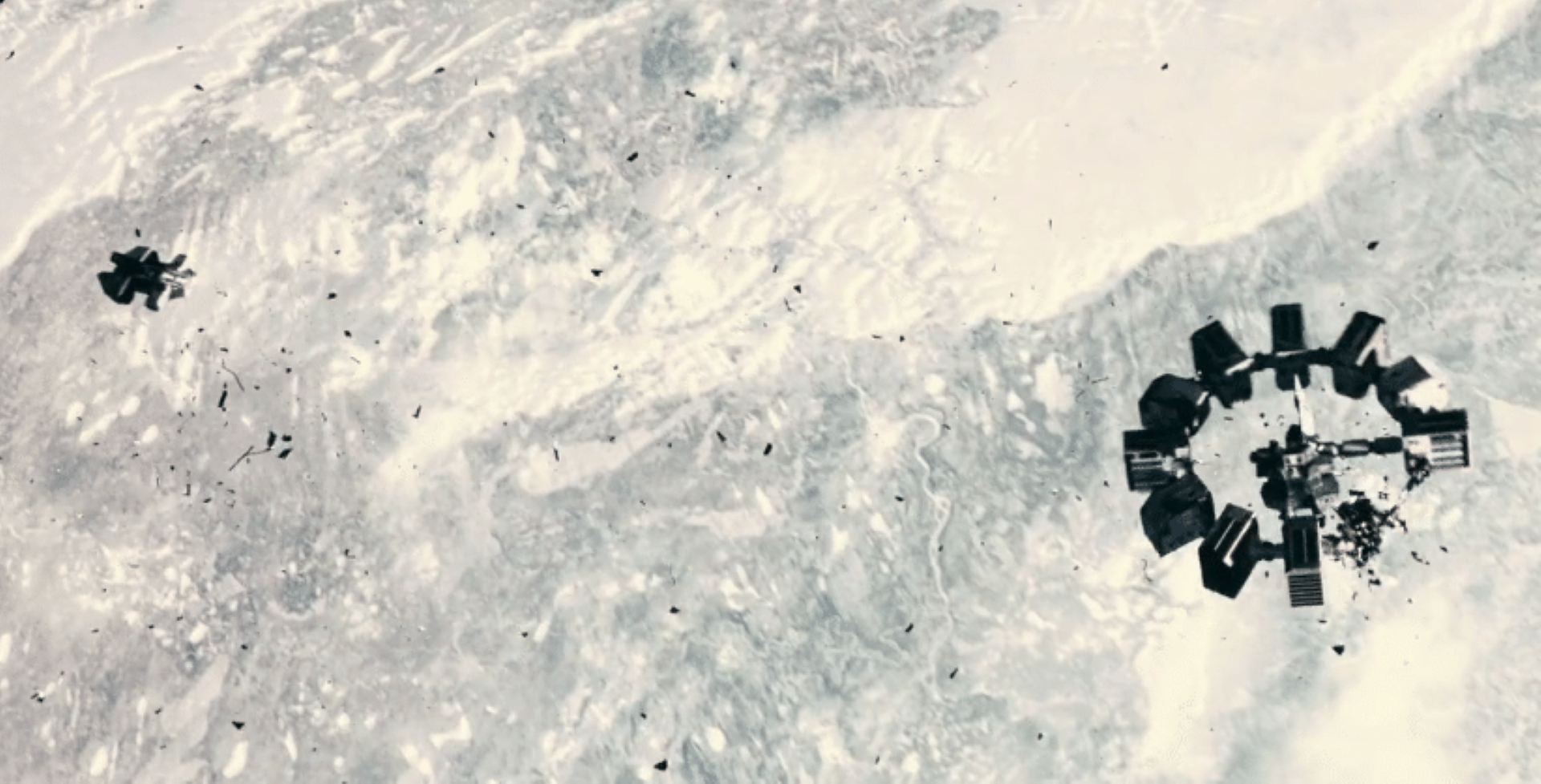 Rys. a. Kadr z filmu przedstawia stację kosmiczną, która znajduje się z prawej strony zdjęcia. Stacja ma kształt dużego pierścienia, na którym zamocowano w równych odległościach 12 prostopadłościennych komór. Dziesięć komór jest w dobrym stanie, a z dwóch komór leżących obok siebie na skutek wybuchu zostały tylko małe fragmenty. Na lewo od stacji kosmicznej widoczny jest znacznie od niej mniejszy statek kosmiczny o nieregularnym kształcie. Przestrzeń między stacją i statkiem wypełniają liczne małe odłamki powstałe po wybuchu na stacji. 