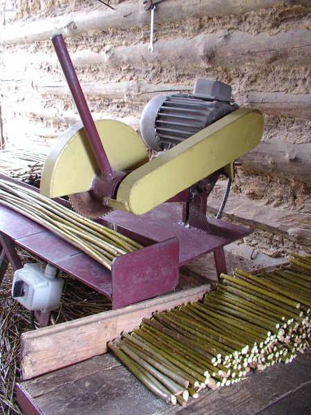 Zdjęcie urządzenia do przycinania zrzezów. Urządzenie składa się z metalowego blatu oraz umieszczonej nad nim konstrukcji z ramieniem zakończonym tarczą tnącą zasilaną silnikiem. Ramię to posiada uchwyt, który umożliwia opuszczanie tarczy podczas cięcia. Obok urządzenia znajduje się stos równo przyciętych zrzezów.
Nagranie tożsame z treścią opisu.