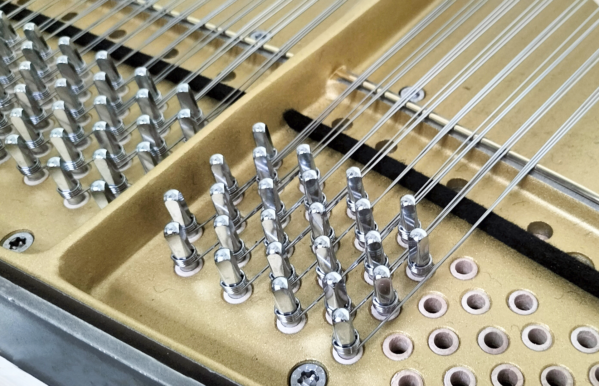 Zdjęcie przedstawia fragment strojnicy z metalowymi kołkami stroikowymi, od których odchodzą wiązki drutów stalowych.