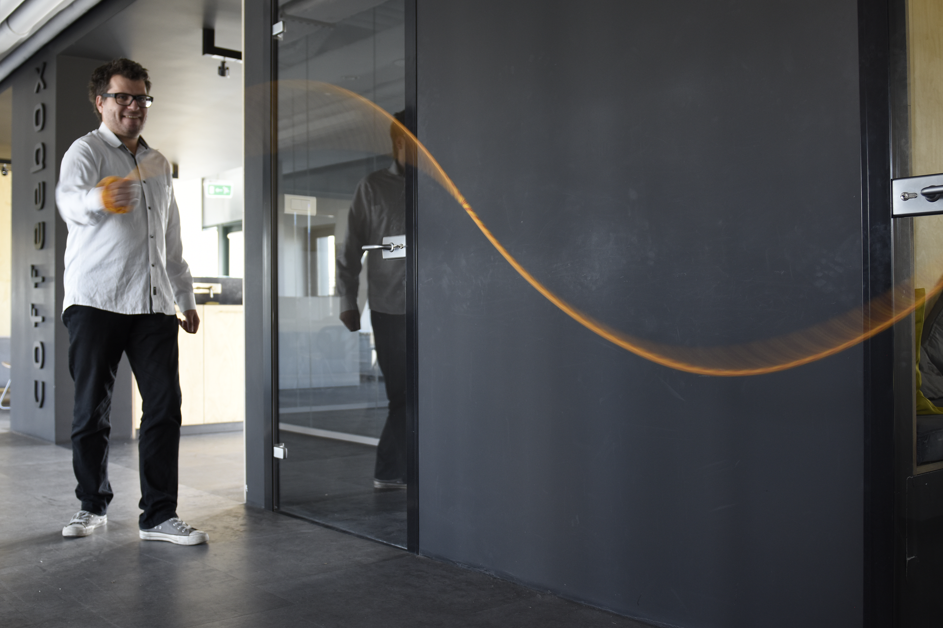 Zdjęcie ukazuje mężczyznę w okularach szybko poruszającego poziomo ustawioną liną. W tle szare ściany wnętrza budynku. Lina w kolorze pomarańczowym układa się w linię falistą o jednej górce i jednej dolince.