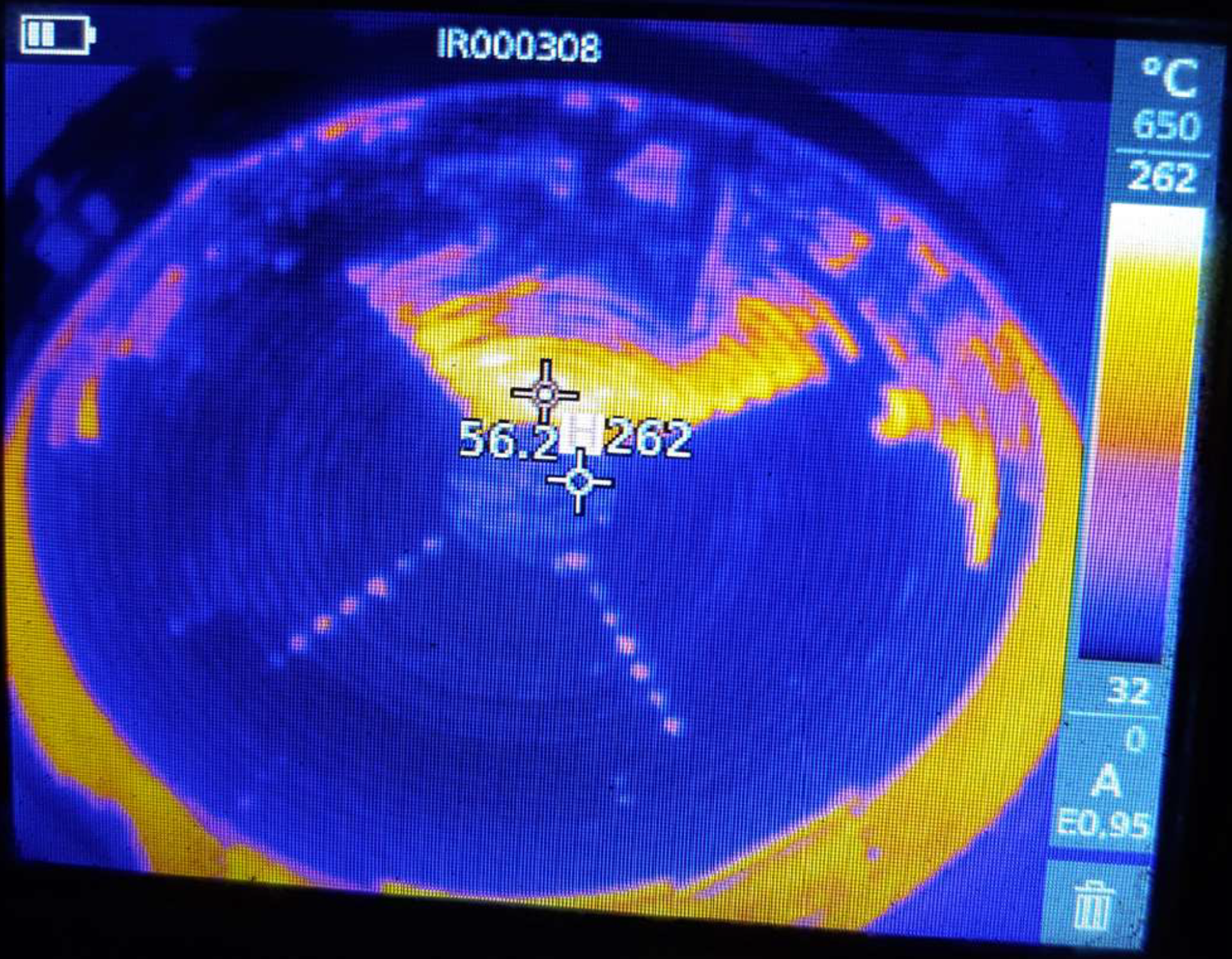 Na zdjęciu termograficznym widnieje anomalia w przepływie wody przez ekran chłodzący naczynia próżniowego do odgazowywania stali. Na środku grafiki znajduje się niebieskie koło, które otoczone jest żółtym światłem. W środku okręgu są żółte oraz fioletowe plamki. Po prawej stronie zdjęcia znajduje się pionowy pasek z temperaturą oraz pomiarami.