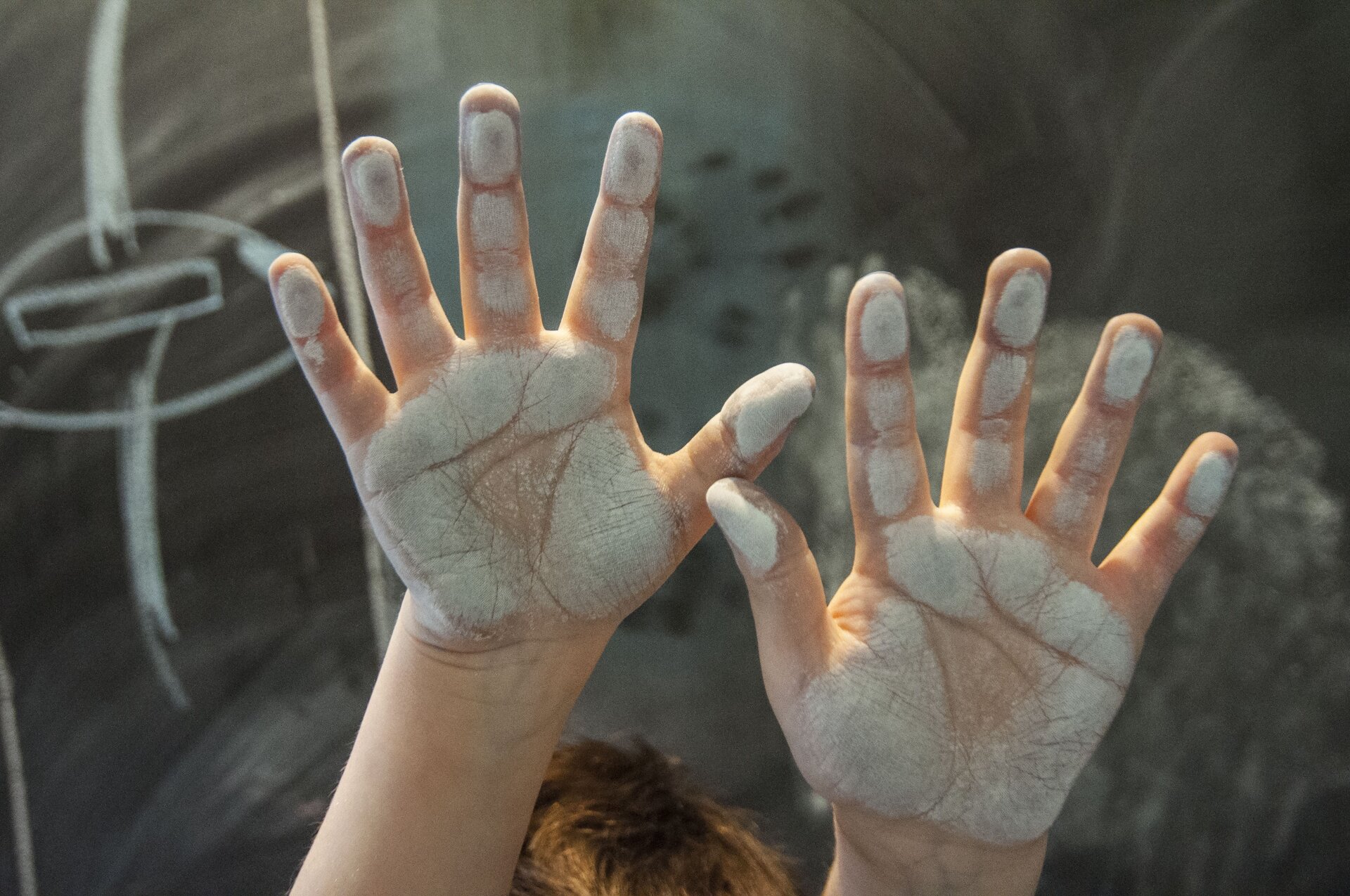 Ilustracja przedstawia dwie dziecięce dłonie, pomalowane białą farbą. Tło fotografii jest szare. Ukazuje abstrakcyjne plamy.