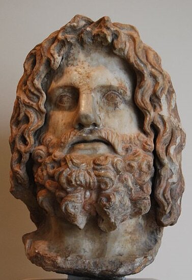 Zdjęcie przedstawia rzeźbę - głowę mężczyzny. Ma dłuższe kręcone włosy oraz brodę.   