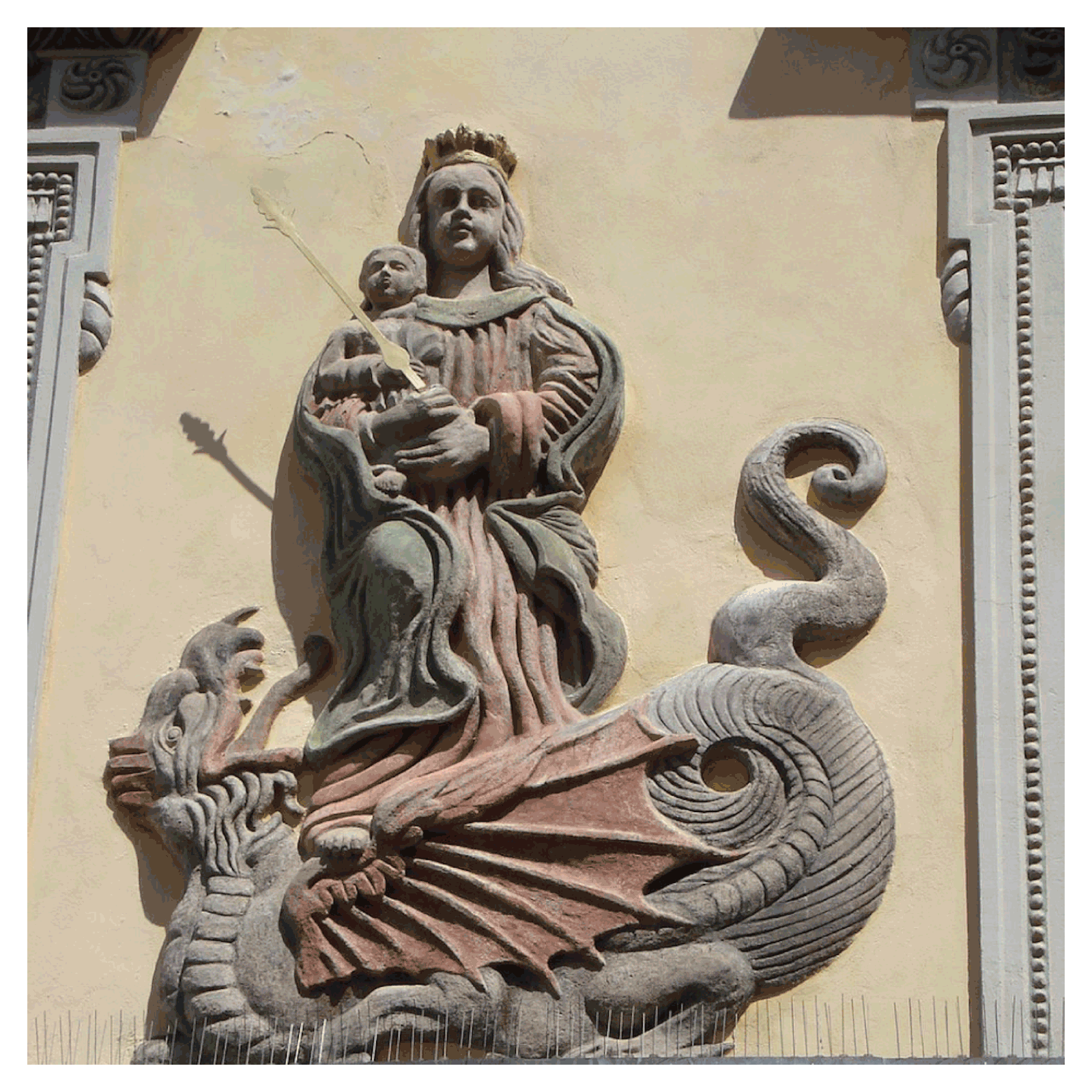 Zdjęcie przedstawia rzeźbę Matki Boskiej z Dzieciątkiem. To relief, rzeźba wykonana na ścianie budynku. 