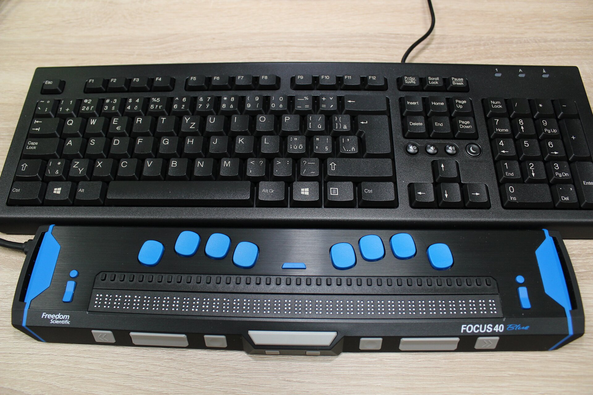 Na zdjęciu widać klawiaturę do komputera ze standardowymi klawiszami. Poniżej, równolegle do klawiatury, leży podłużny przyrząd o kształcie prostopadłościanu. Na frontowej ścianie znajduje się rząd zapisany pismem Braille'a, nad każdą literą zapisaną brailem znajduje się prostokątny, czarny przycisk. Wyżej widać dwie grupy po cztery niebieskie przyciski, ułożone tak, by łatwo było oprzeć o nie palce obu rąk. Na urządzeniu widać napis: FOKUS 40.