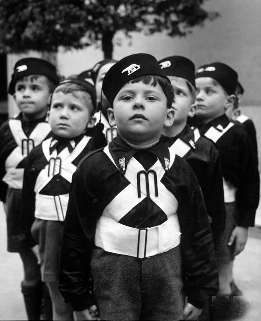 Na zdjęciu grupa dzieci w mundurkach. Dzieci stoją na baczność. Mundurki są przepasane skrzyżowanymi pasami. Dzieci noszą berety.