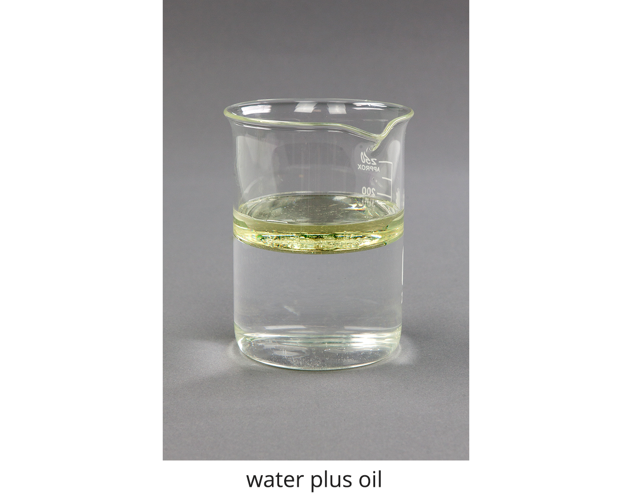 Zdjęcie przedstawia zlewkę wypełnioną wodą oraz olejem, water plus oil. Warstwa oleju nie miesza się z wodą, pozostaje na powierzchni wody. 