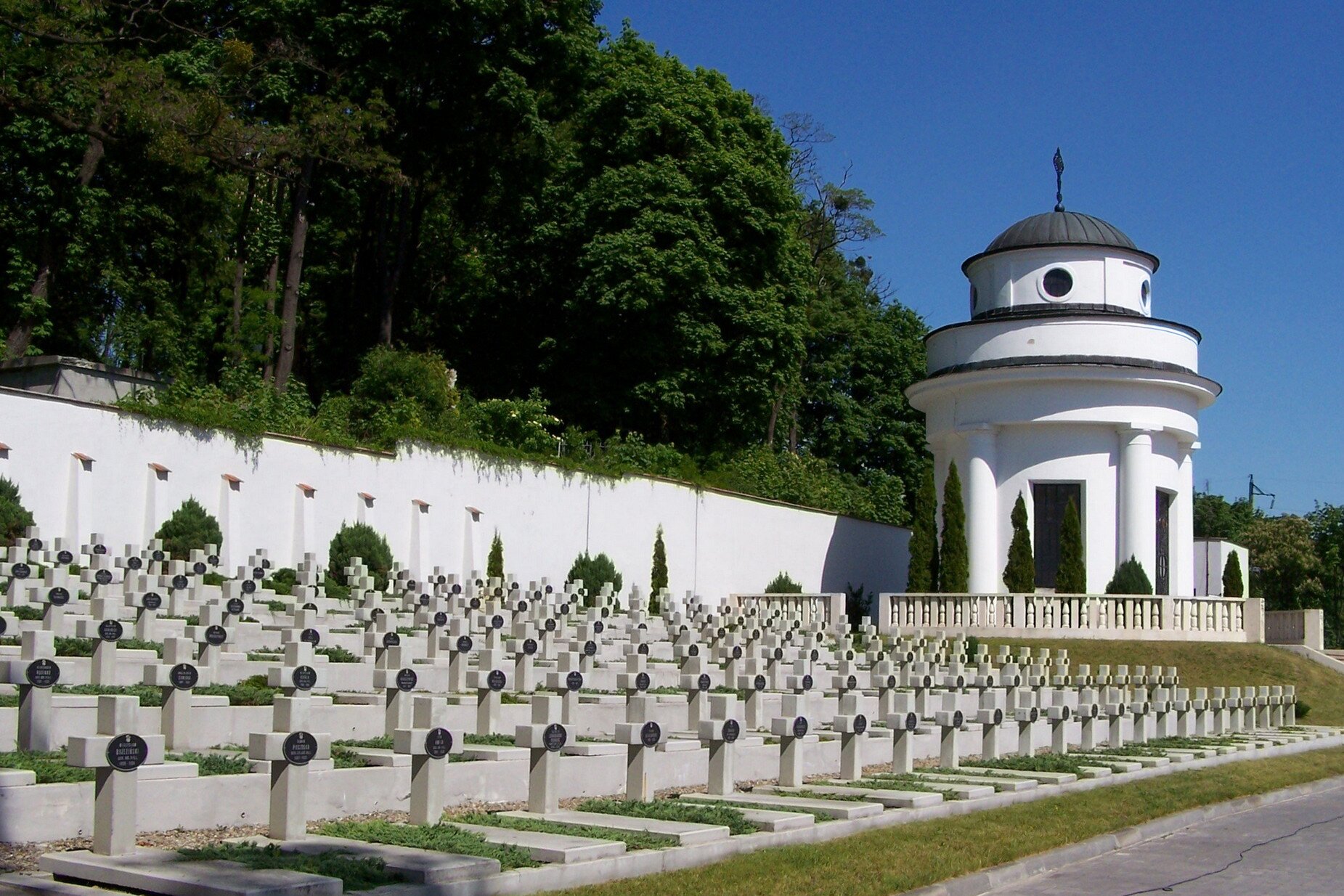 Kliknij, aby powiększyć Zdjęcie przedstawia czysty i schludny cmentarz. Nagrobki są wykonane identycznie. Panuje ład, harmonia.