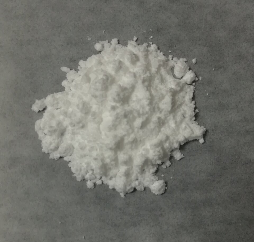 Na rysunku znajduje się biała substancja w postaci proszku. Tło ma barwę szarą.