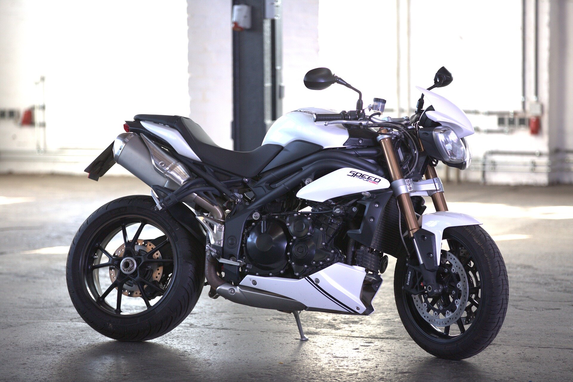 Zdjęcie przedstawia srebrno‑czarny motocykl. Stoi w przestronnej hali. Pojazd ma masywną rurę wydechową. 