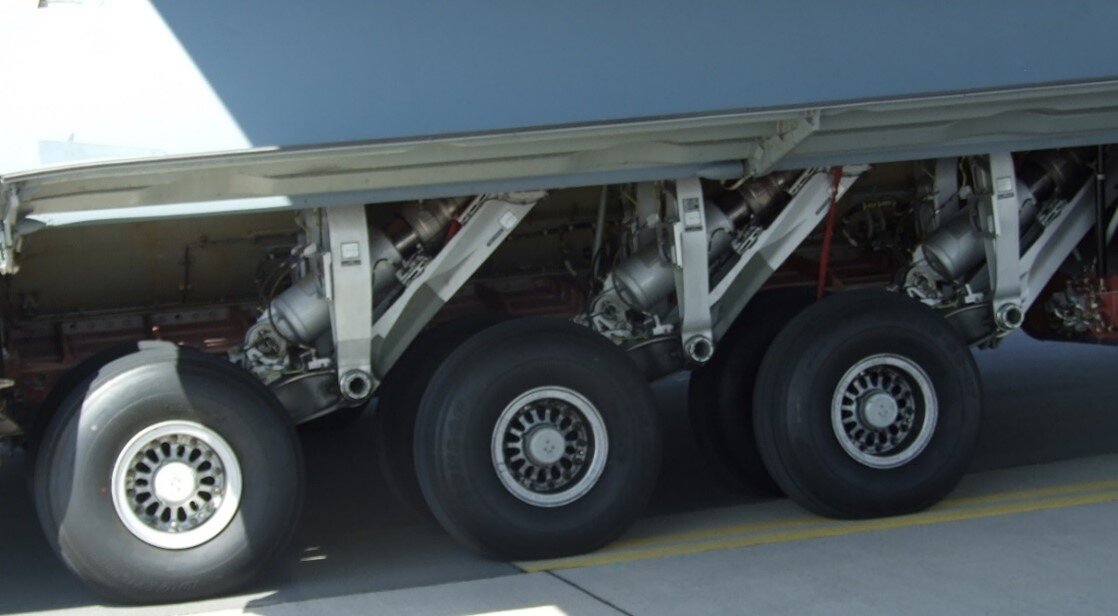 Zdjęcie przedstawia podwozie trójpodporowe samolotu. Widoczne są trzy koła oraz rusztowania na których są one umieszczone. Koła są przymocowane do zawieszenia pod kątem ostrym do kadłuba. Prezentowane podwozie jest podwoziem składanym. 