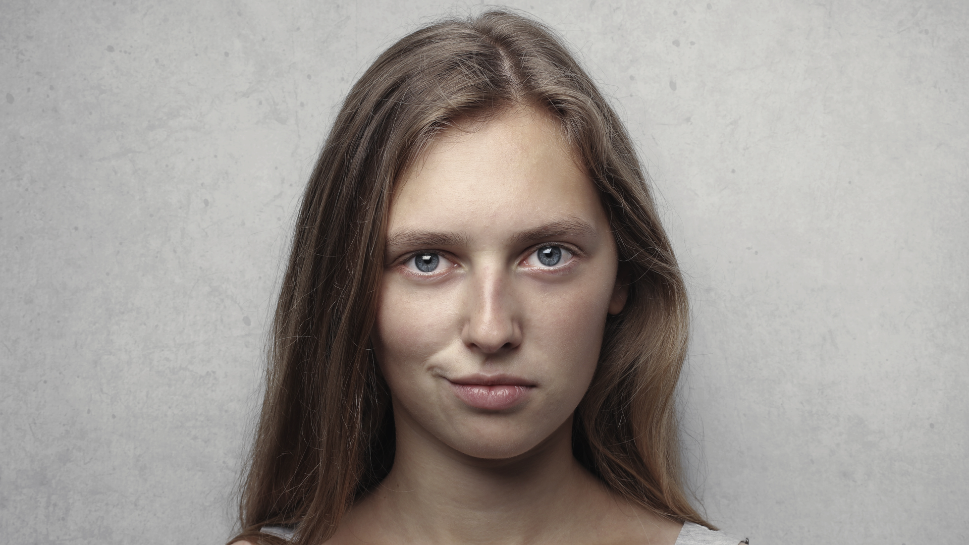 Zdjęcie przedstawiające kobietę patrzącą bezpośrednio w obiektyw. Kobieta delikatnie się uśmiecha podciągając jeden z kącików ust. Kobieta wygląda na zadowoloną z siebie.