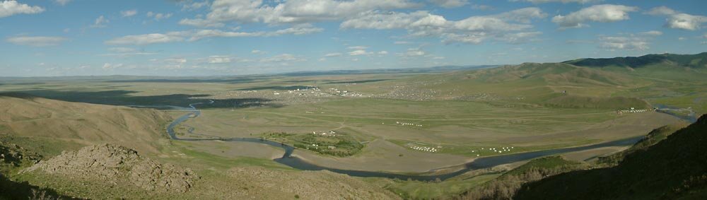 Zdjęcie przedstawia krajobraz nizinny, z korytem rzeki. W oddali zabudowania.