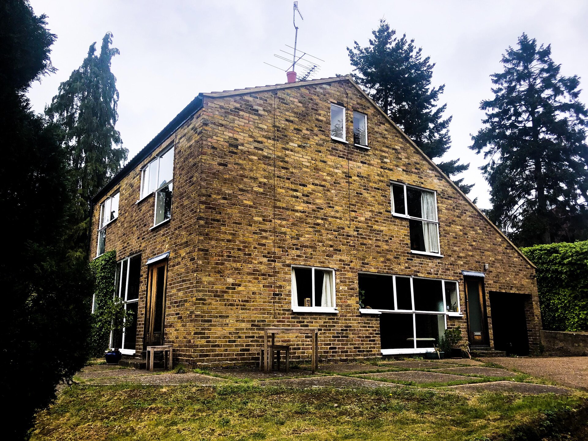 Fotografia przedstawia dom zbudowany z żółtej cegły. Ma on prosty kształt - prostopadłościanu z dachem dwuspadowym. Jedna strona dachu opada niżej niż druga. Okna w domu rozłożone są w podobnych odstępach.