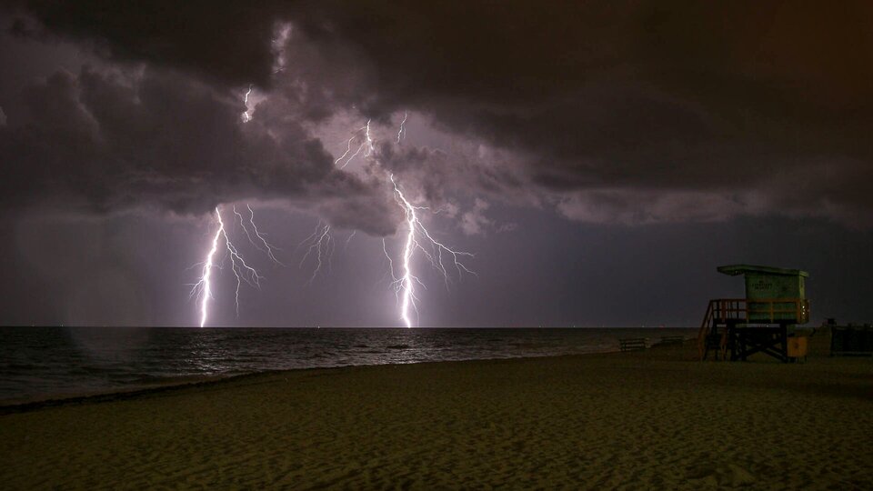Zdjęcie przedstawia zachmurzone, ciemne niebo, które rozświetlają pioruny. Mają one kształt linii prostych i rozgałęzionych. Sięgają od chmur po horyzont. 