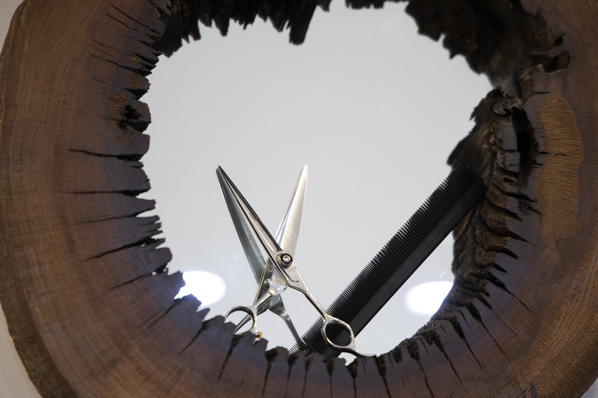 Zdjęcie przedstawia lustro w drewnianej ramie. O lustro oparte są nożyczki i grzebień.