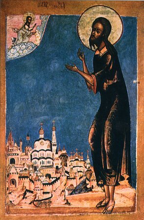 Kliknij żeby powiększyć Na ilustracji znajduje się ikona św. Aleksego. Duża postać Aleksego stoi przed małym miastem z elementami architektury typowej dla Wschodu. Święty ma czarne włosy i brodę w tym samym kolorze. Nad głową znajduje się aureola. Jest ubrany w ciemnobrązową szatę. Na nogach ma sandały. W górnym prawym rogu ikony znajduje się mały obrazek. Przedstawia Aleksego w jasnej szacie. Nad głową ma aureolę. Klęczy. Rękami dotyka złota.