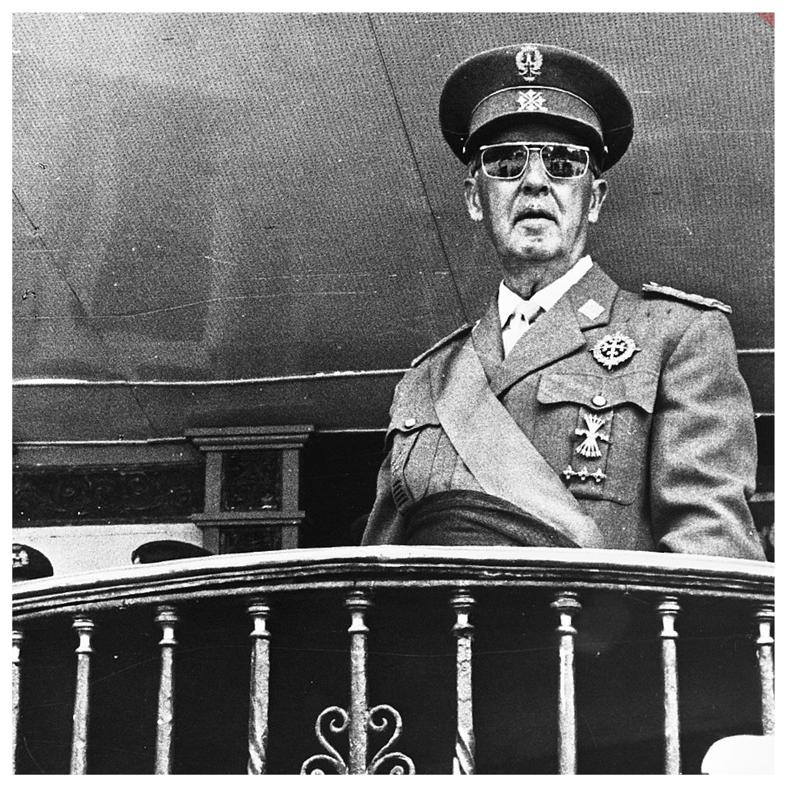 Zdjęcie przedstawia dojrzałego mężczyznę w mundurze i okularach przeciwsłonecznych. Za nim widoczni są jeszcze inni mężczyźni w mundurach.