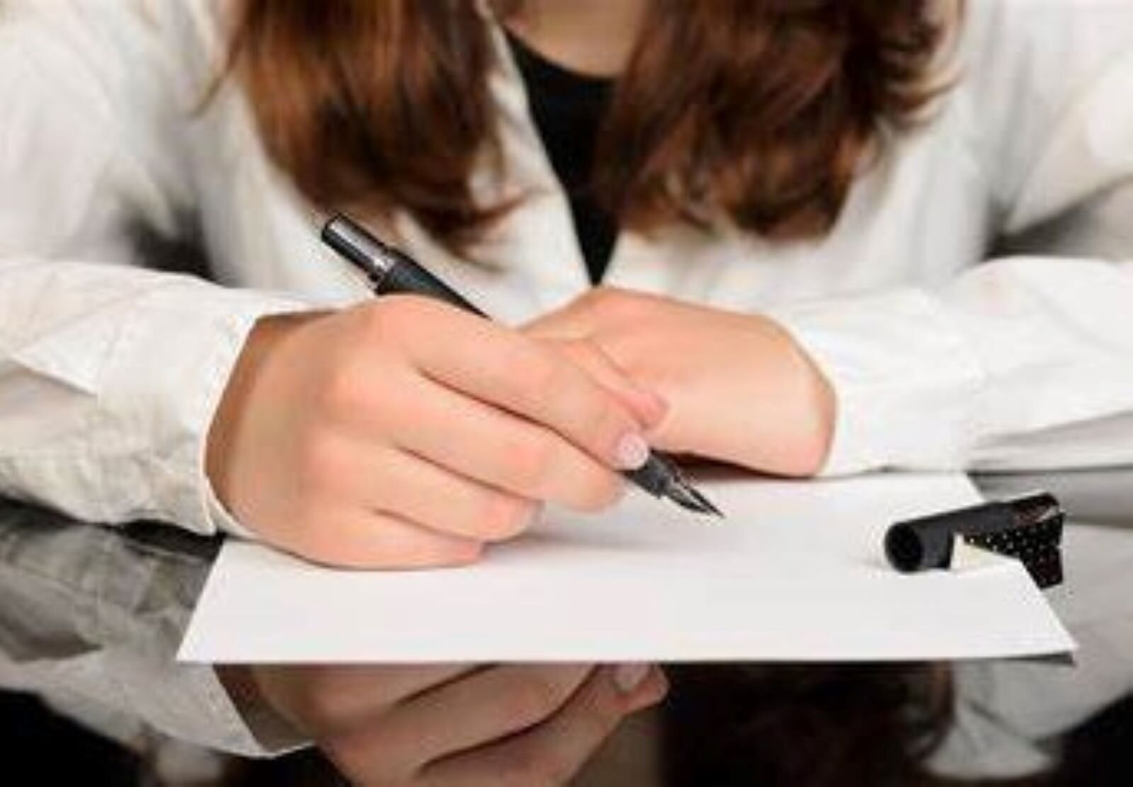 Zdjęcie przedstawia pochyloną nad zeszytem dziewczynę, trzymającą w ręku pióro, która porządkuje i podsumowuje zebrane informacje.