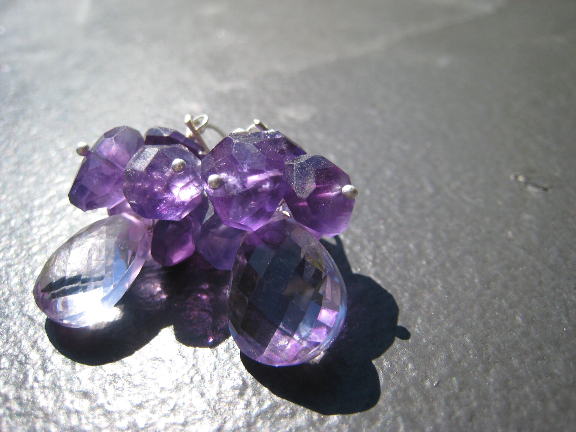 Na zdjęciu widoczna jest biżuteria wykonana z kilkunastu niewielkich ametystów połączonych ze sobą w coś w rodzaju bukietu. Wszystkie kamienie mają fioletowy kolor, za wyjątkiem silnie podświetlonego po lewej stronie, który wydaje się przezroczysty i bezbarwny. Kamienie połączone są ze sobą za pomocą metalowych drucików.