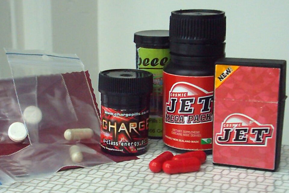 Zdjęcie przedstawia dopalacze w zakręcanych plastikowych opakowaniach. Na etykietach jest napis cosmic jet. Obok opakowań w zamykanych małych woreczkach są zamknięte pojedynczo tabletki i kapsułki. 