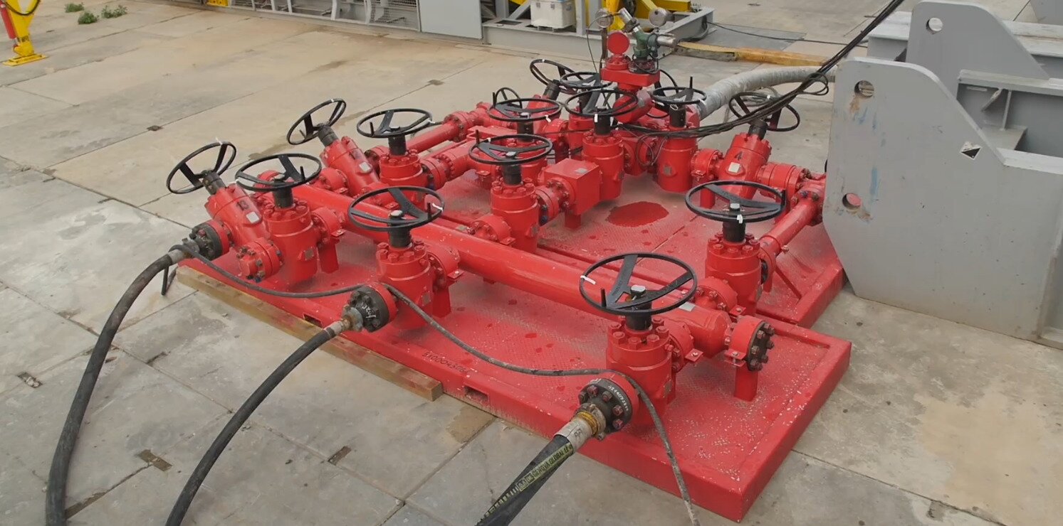 Na zdjęciu widoczny jest węzeł dławienia. Węzeł dławienia służy do tłumienia wypływu płynu złożowego z otworu. Na zdjęciu widoczna jest platforma, na której znajduje się duża ilość przewodów z zaworami. Z jednej strony do węzła prowadzą trzy przewody, a z drugiej znajduje się jeden większy przewód. Przy większym przewodzie znajdują się manometry. Węzeł dławienia posiada dużo więcej zaworów niż węzeł zatłaczania.Poniżej zdjęcia w prawym dolnym rogu widoczny jest przycisk odtwarzania. Tekst nagrania jest zgodny z tytułem zdjęcia.