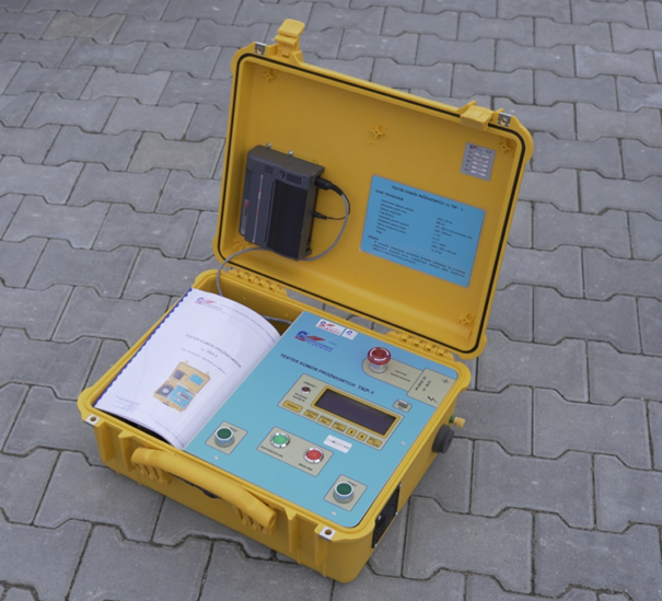 Ilustracja przedstawia tester komór próżniowych typ TKP‑1. Urządzenie wbudowane jest w żółtą plastikową skrzynkę z uchwytem. 