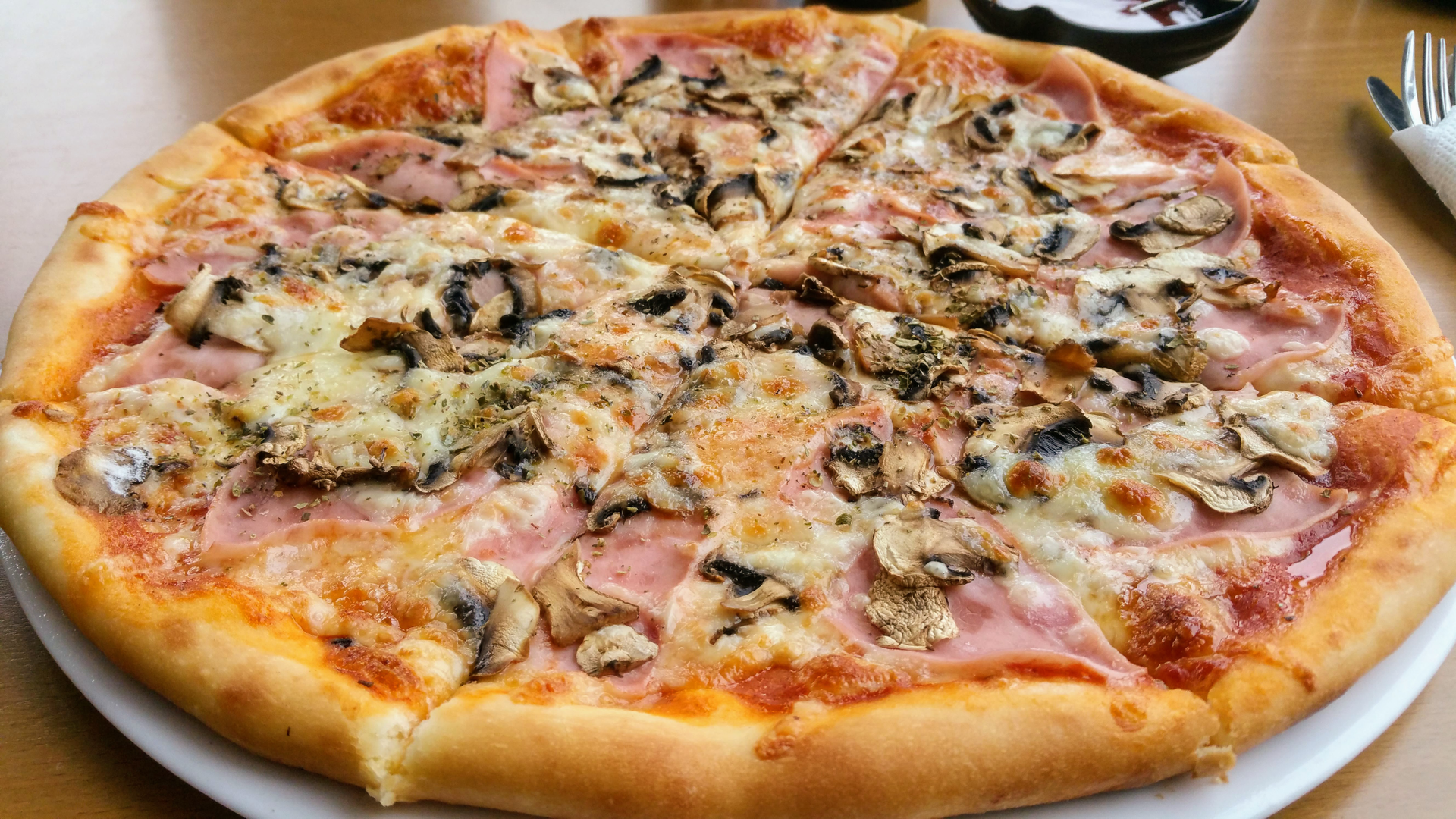 Zdjęcie przedstawia pizzę z pieczarkami, serem i szynką. Pizza znajduje się na talerzu.