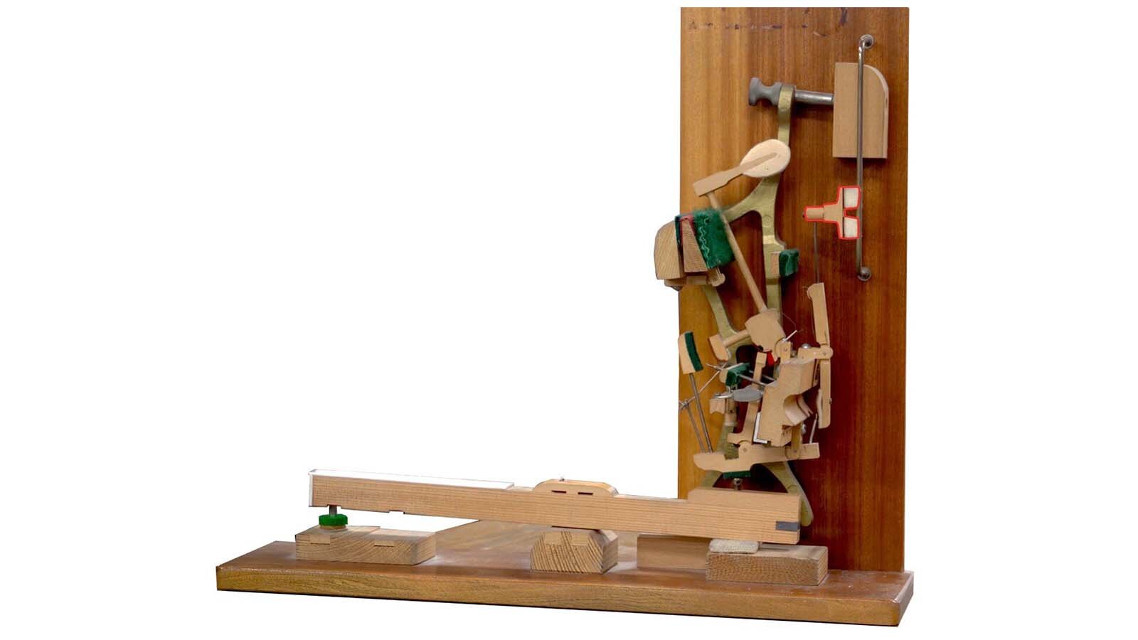 Zdjęcie przedstawia mechanizm pianina z zaznaczonym czerwoną obwódką tłumikiem. 