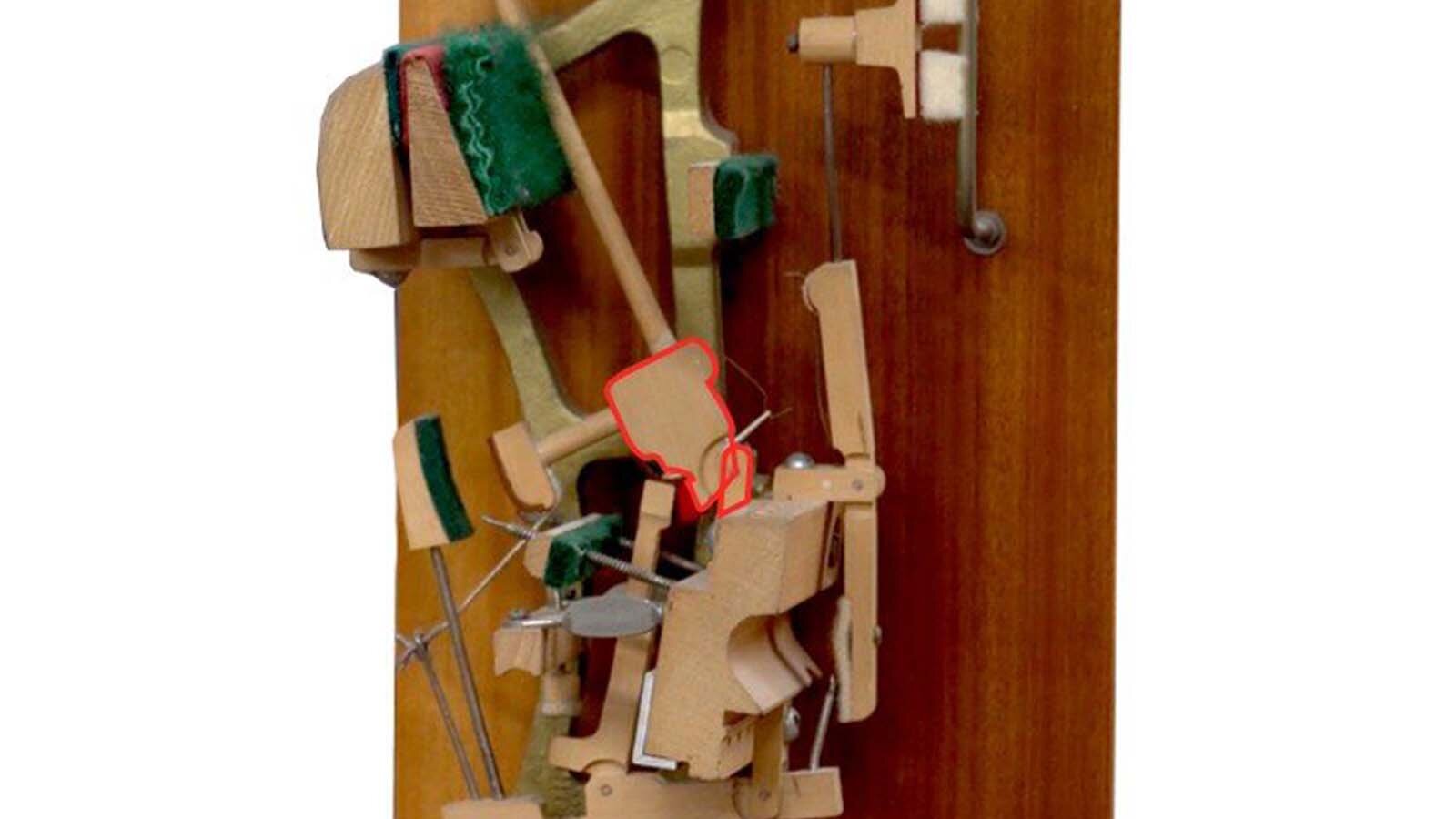 Zdjęcie przedstawia podzespół mechanizmu pianinowego lub fortepianowego jakim jest dźwignia orzechowa. Element został zaznaczony czerwoną obwódką.