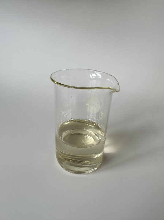 Zdjęcie przedstawia szklane naczynie z przezroczystą cieczą - lakierem akrylowym.