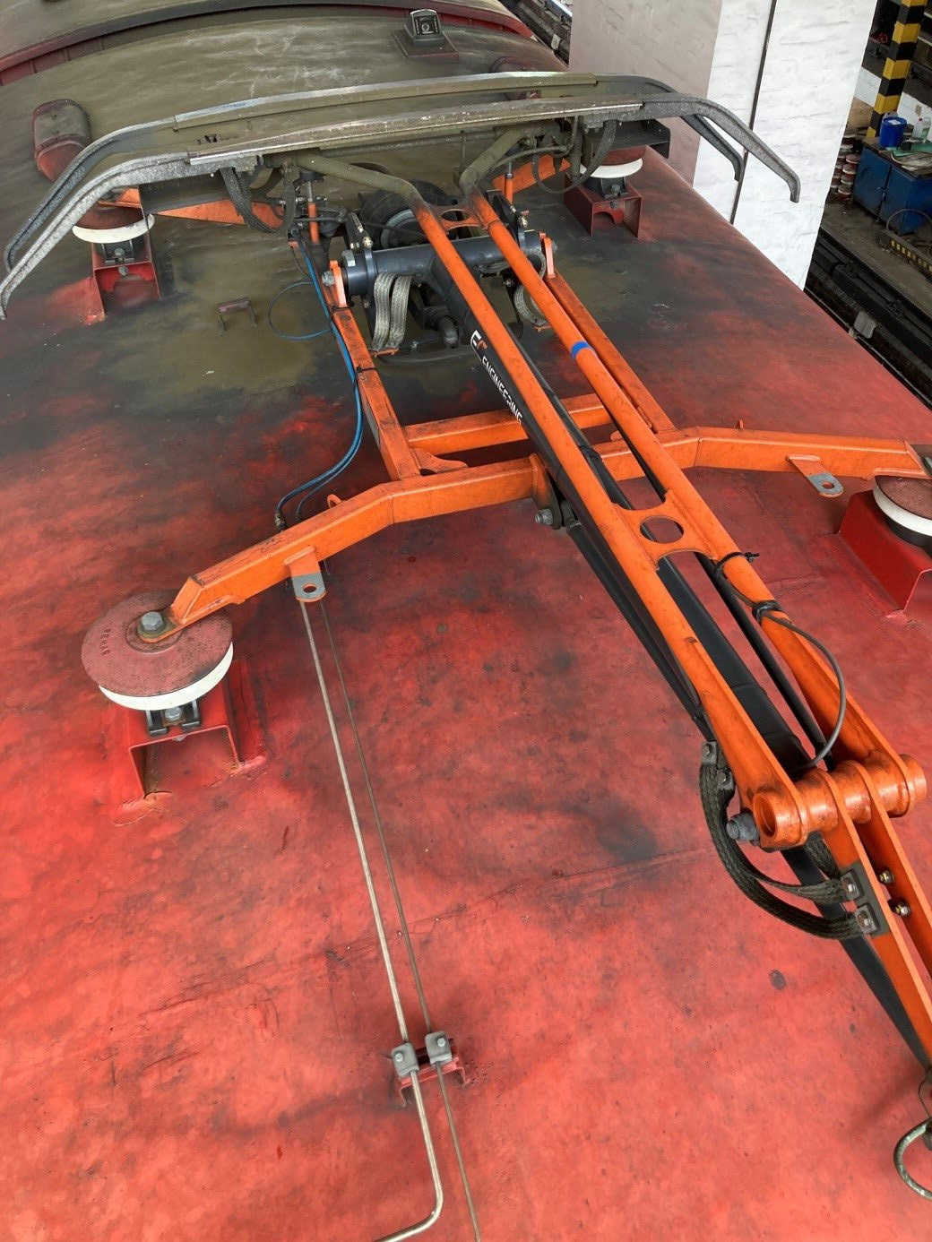 Zdjęcie przedstawia złożony pantograf jednopołówkowy na dachu wagonu. W tej pozycji ma on kształt litery T, nie biorąc pod uwagę podstawy, która ma kształt litery H ustawionej prostopadle do litery T pantografu.