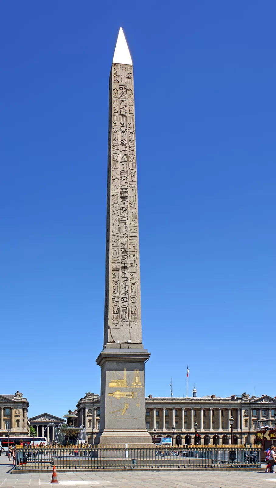 Fotografia przedstawia obelisk stojący na wysokim cokole, na którym znajdują się sceny przedstawiające jego transport - wyryte obrazy pokazują dźwigary, obelisk oraz specjalne tory, którymi bym transportowany. Powierzchnia obelisku pokryta jest hieroglifami przedstawiającymi sceny z życia codziennego. Obelisk ma błyszczące zwieńczenie w kształcie trójkąta. Jest ogrodzony i stoi na placu miejskim. 