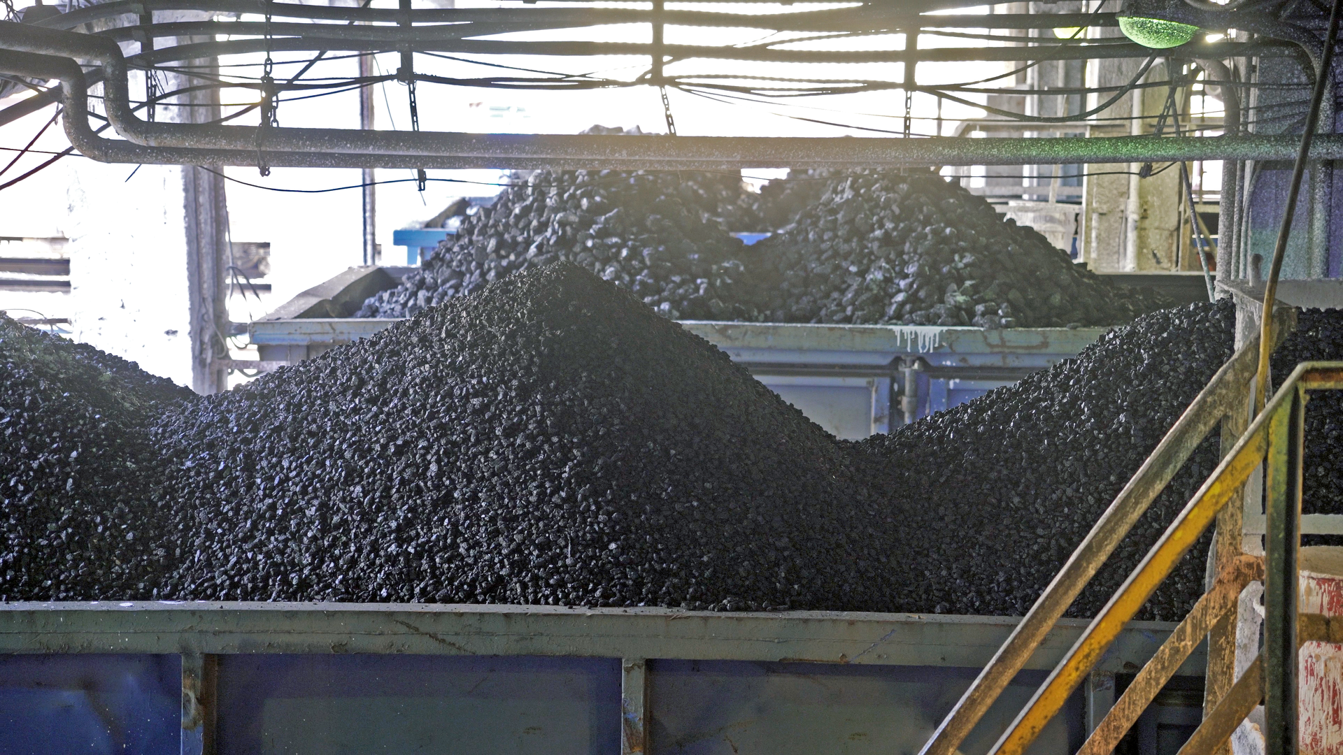 Na zdjęciu widoczny jest proces ładowania węgla na wagony. W centralnej części ekranu widoczne są dwa wagony załadowane węglem. Nad wagonami widoczne są zielone rury i okablowanie. Po prawej stronie ekranu widać filary.