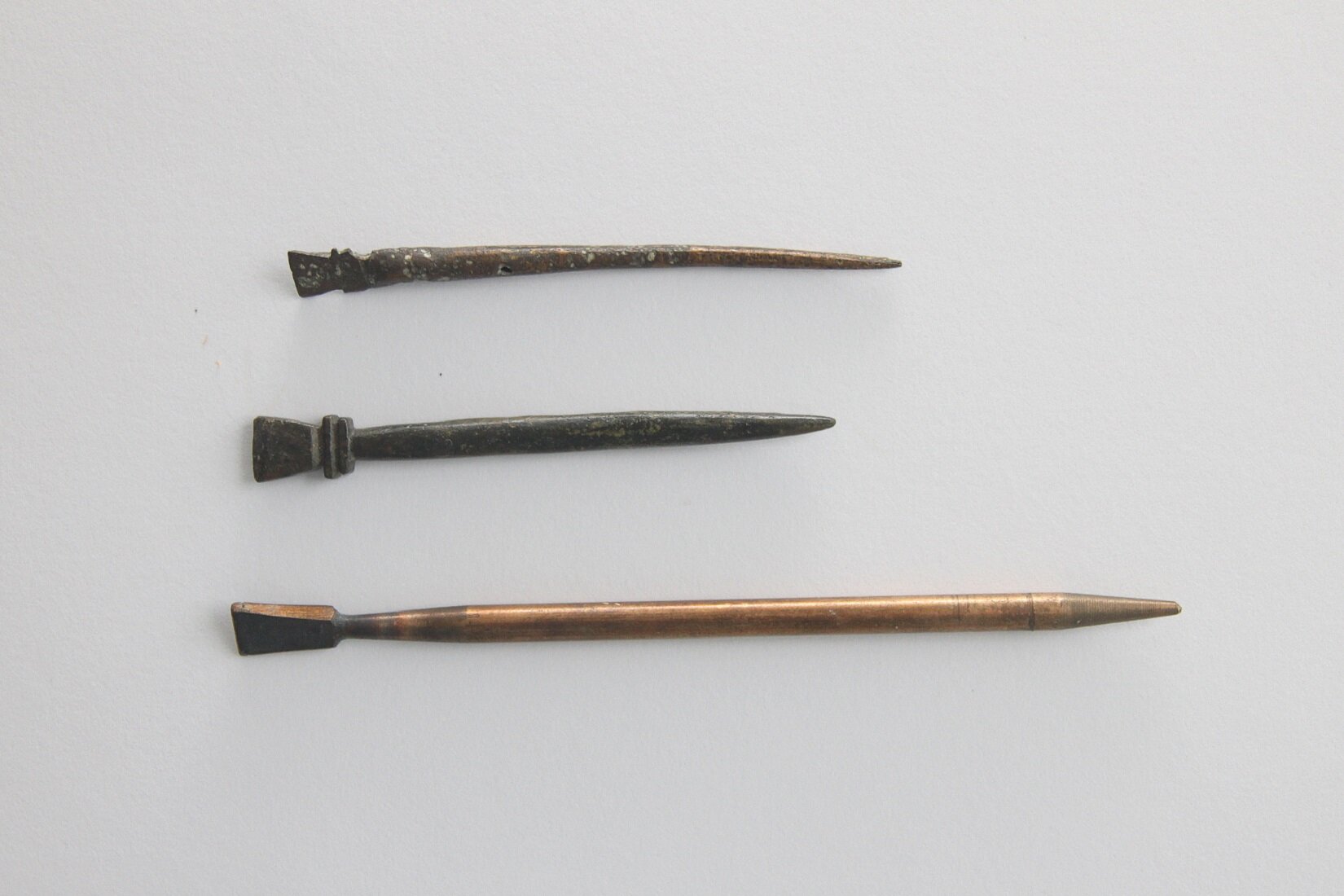 Zdjęcie przedstawia trzy podłużne, cienkie przyrządy z ostrym zakończeniem. Wykonane są z metalu. Każdy różni się długością i kolorem. Ułożone są na białym tle.