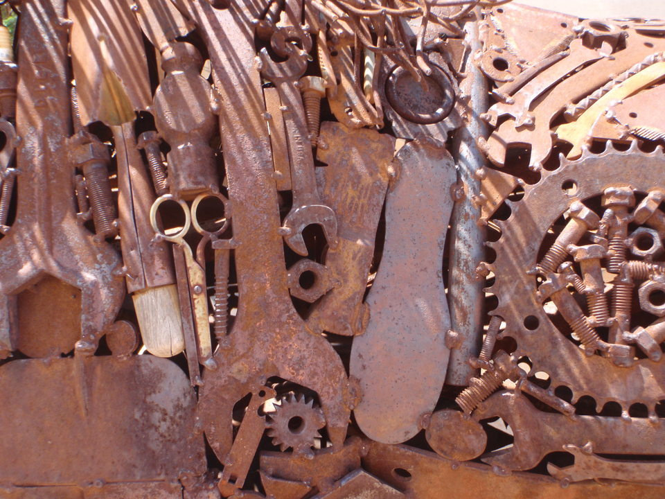 Na zdjęciu widoczne są metalowe przedmioty pokryte rdzą, takie jak nożyczki, koła zębate, śrubki, klucze hydrauliczne. 