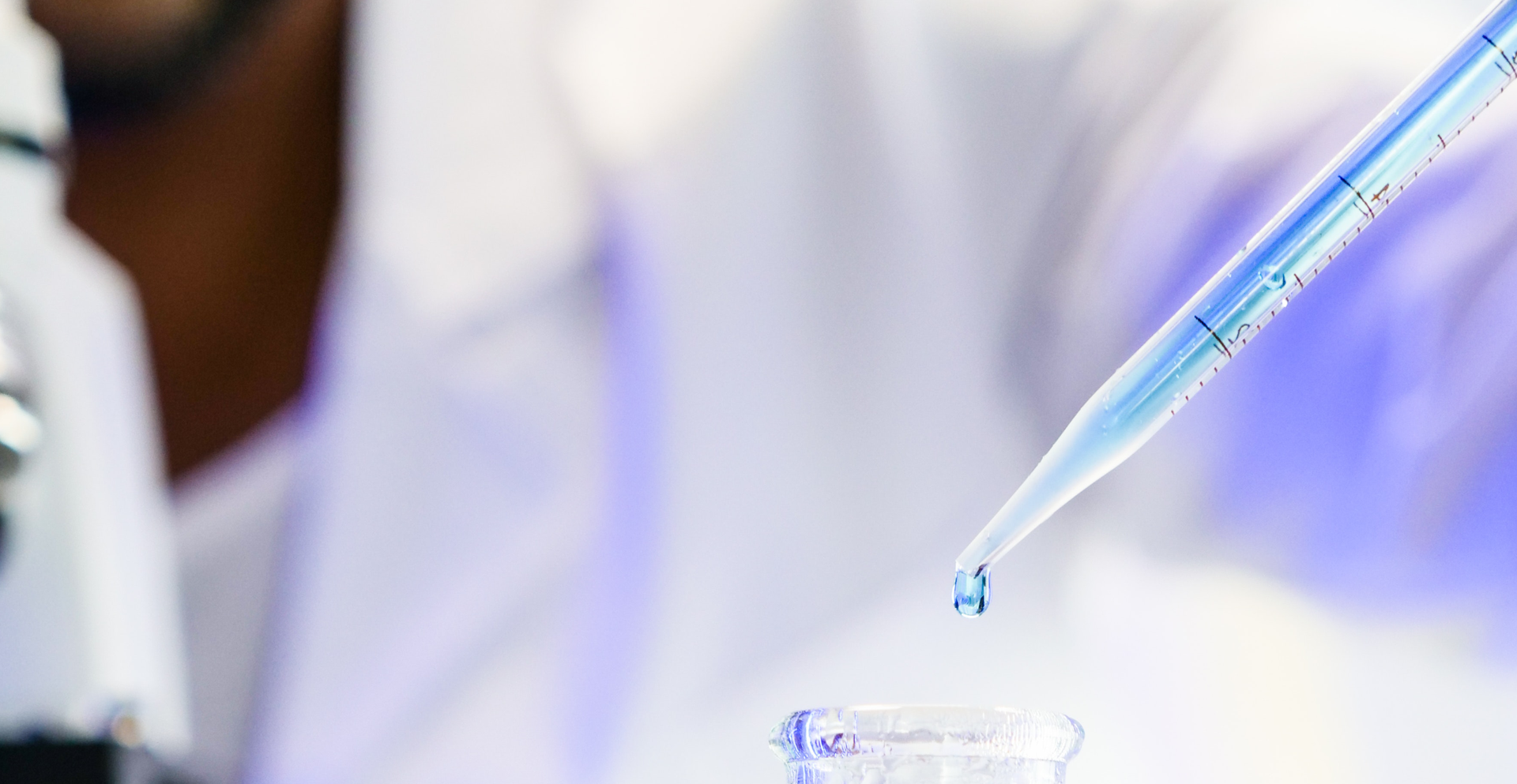 Zdjęcie przedstawia zbliżenie na pipetę. Na końcu pipety widoczna jest kropla płynu.