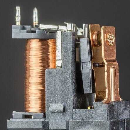 Grafika przedstawia przekaźnik elektromagnetyczny, czyli urządzenie z miedzianymi zwojami i innymi elementami składowymi.