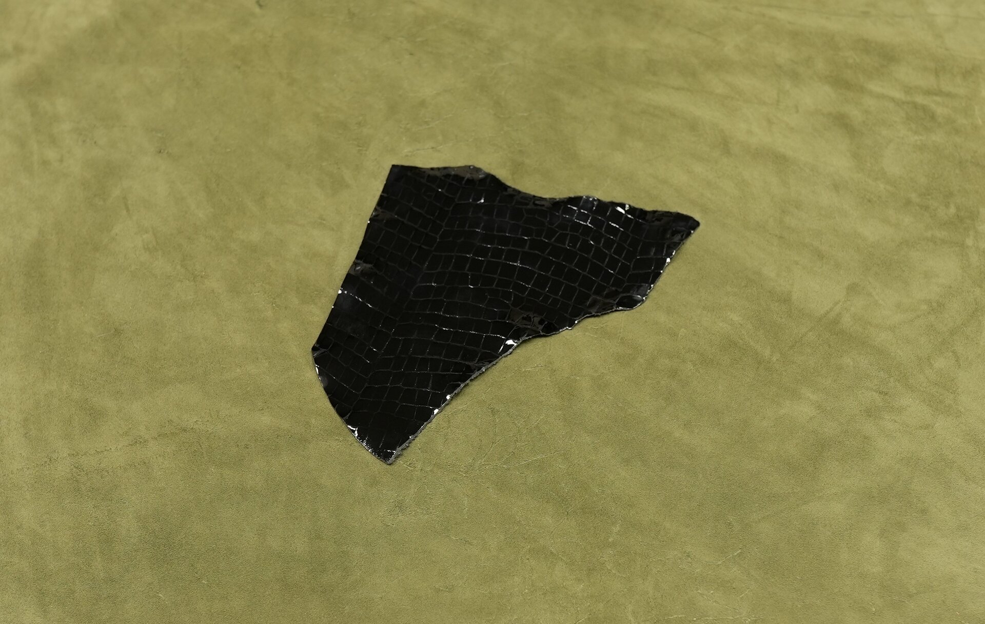 Zdjęcie przedstawia fragment czarnej skóry wykończonej od strony lica lakierem. Powierzchnia skóry ma wysoki połysk.