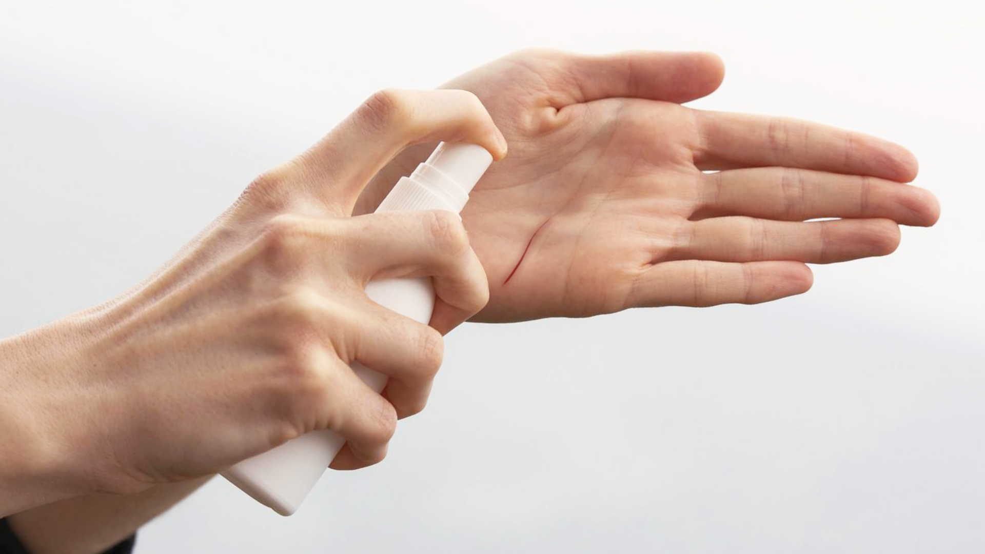 Zdjęcie przedstawia dłonie osoby. W jednej dłoni osoba trzyma pojemnik z atomizerem kierując nim w drugą dłoń.