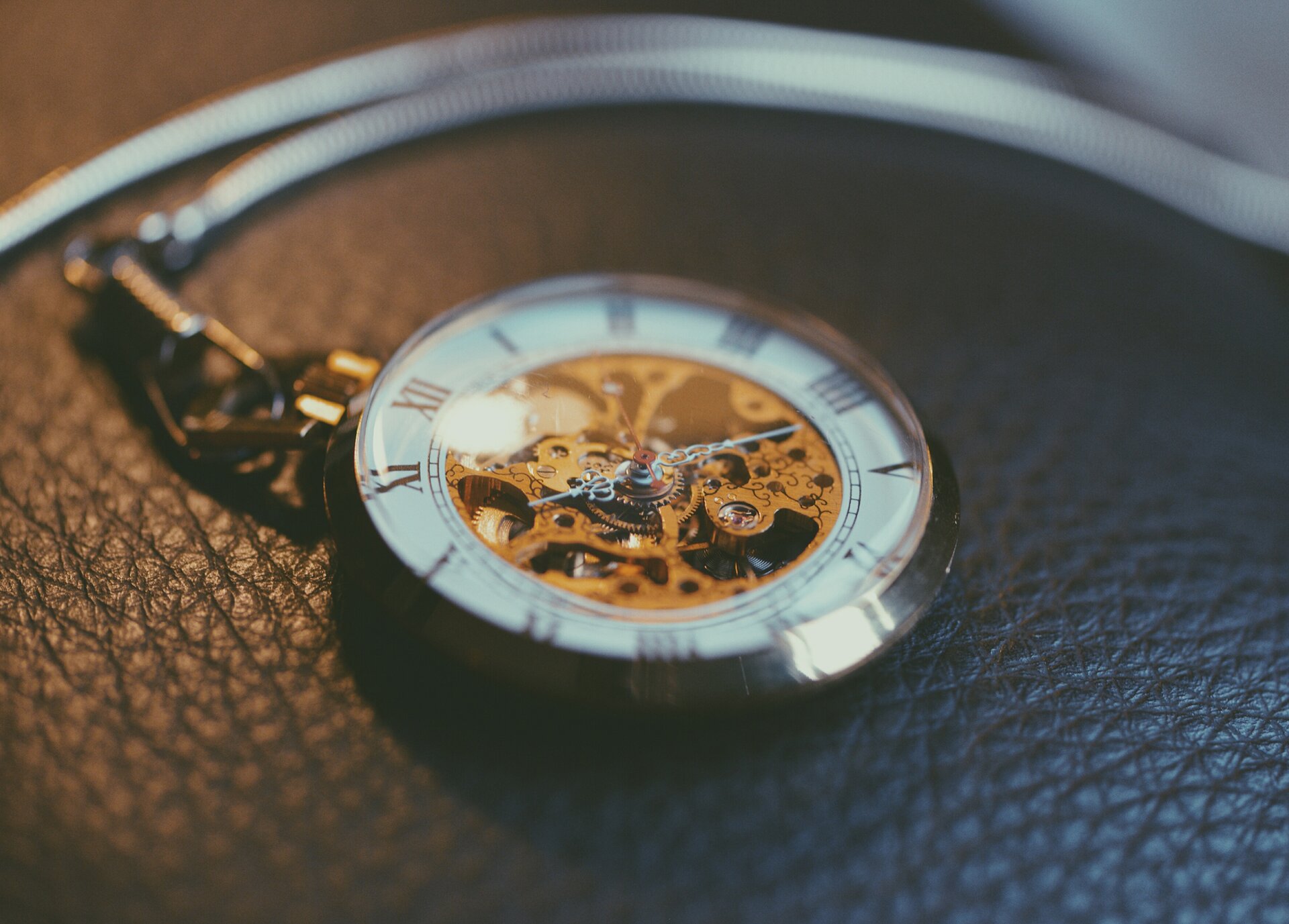 Na zdjęciu mały okrągły zegarek wskazówkowy w srebrnej obudowie z krótkim łańcuszkiem, do którego przyczepiona jest tasiemka lub smycz do kluczy. Ma białą tarczę z rzymskimi cyframi, ozdobna wskazówka zatrzymała się  na godzinie 10.16. Środek tarczy wykonany jest ze szkła, dzięki czemu widać mechanizm ukryty wewnątrz. Zegarek leży na skórzanej powierzchni, być może na oparciu fotela.