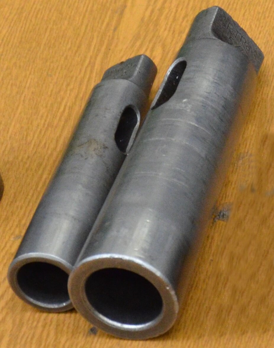 Ilustracja przedstawia tuleje redukcyjne. Są one w kształcie walca, posiadają dwa otwory na dolnej podstawie oraz w górnej części. Górna podstawa jest w kształcie prostopadłościanu opartego na kole. 