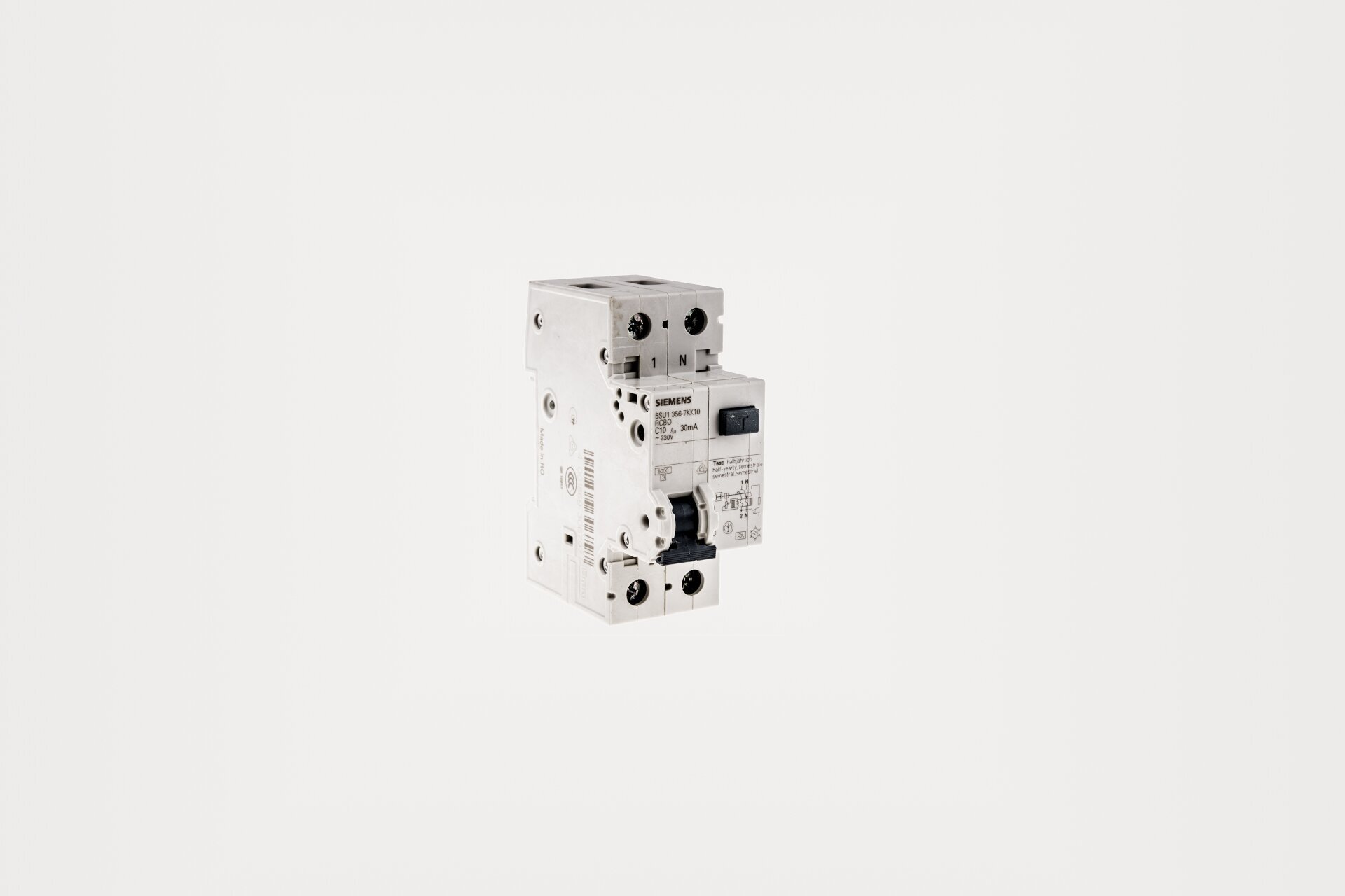 Ilustracja przedstawia bezpiecznik różnicowoprądowy. Jego obudowa wykonana jest z tworzywa sztucznego, ma kształt prostopadłościanu, z nieco wysuniętą częścią przednią. Na przedniej powierzchni urządzenia znajduje się czarna klapka klawisza testowego. Widoczne na obudowie bezpiecznika są także liczne opisy, logotypy producenta oraz parametry techniczne.